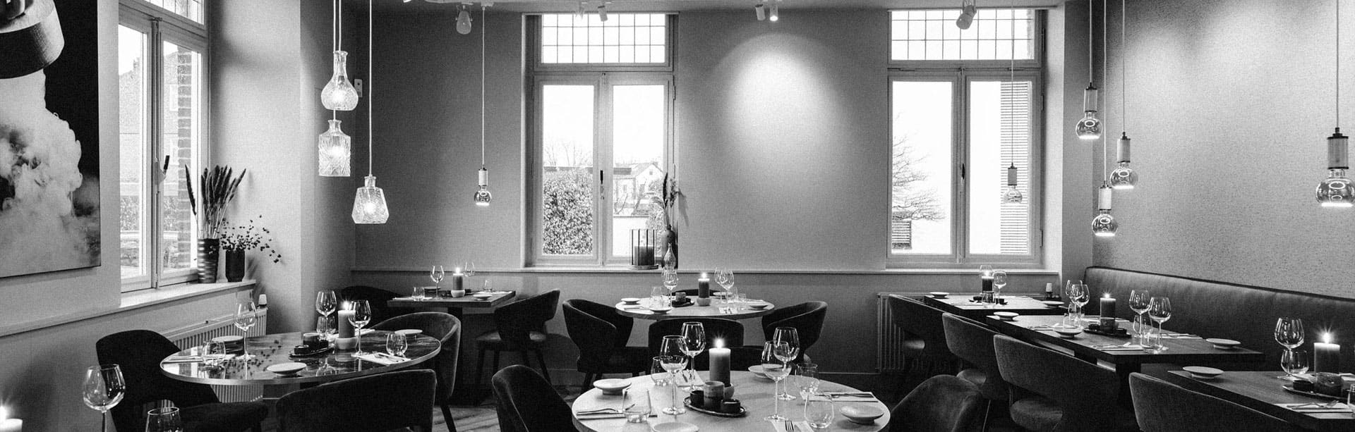 Het sfeervolle interieur van Prix de Rome, met hangende glazen lampen, gedekte tafels en hoge vensters